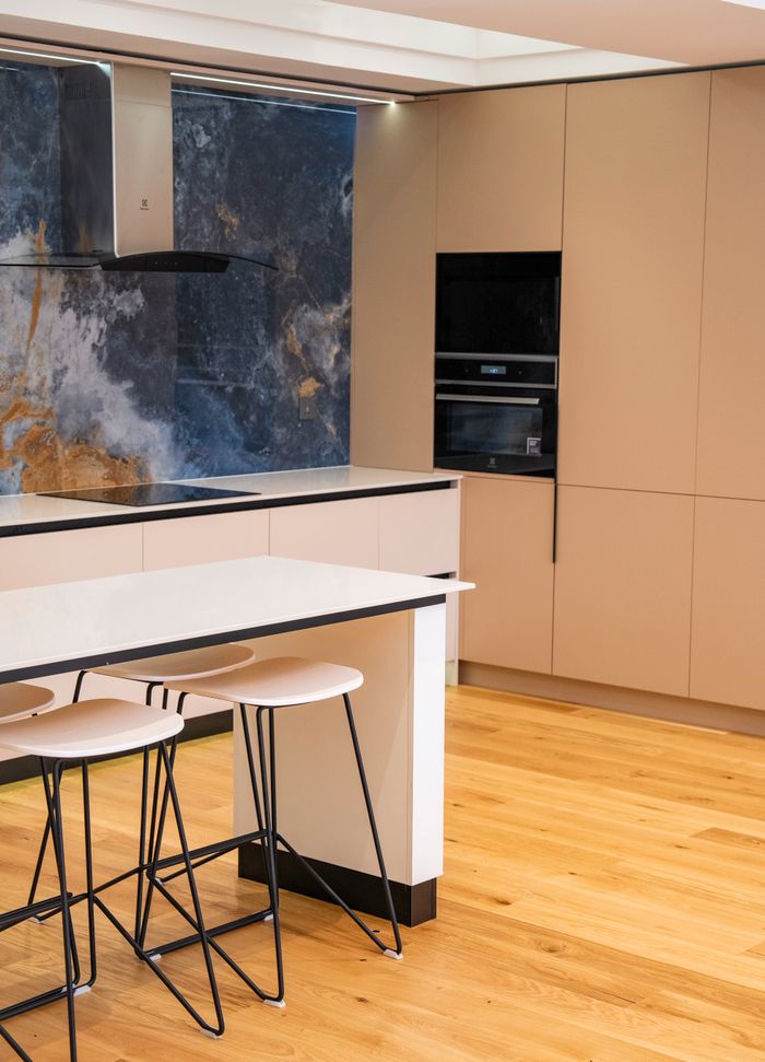 Sleek contemporary kitchen featuring marble backsplash, beige cabinets, and stylish bar stools.